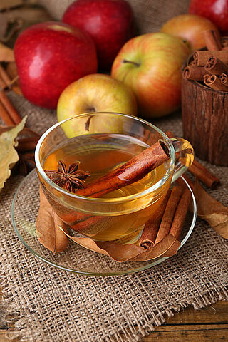 Composition of apple cider with cinnamon sticks, fresh apples and autumn leaves on wooden background