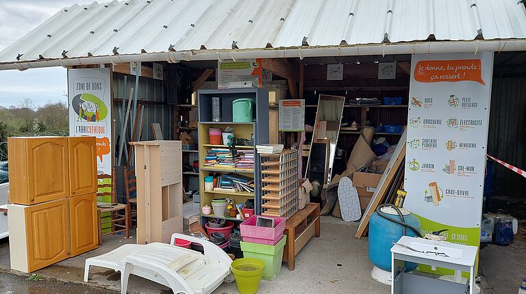 la photo de l'abricothèque représente un abri sous tôle avec des éléments de bricolage et de jardinage en bon état (placard de cuisine, transat, pot de fleur...)